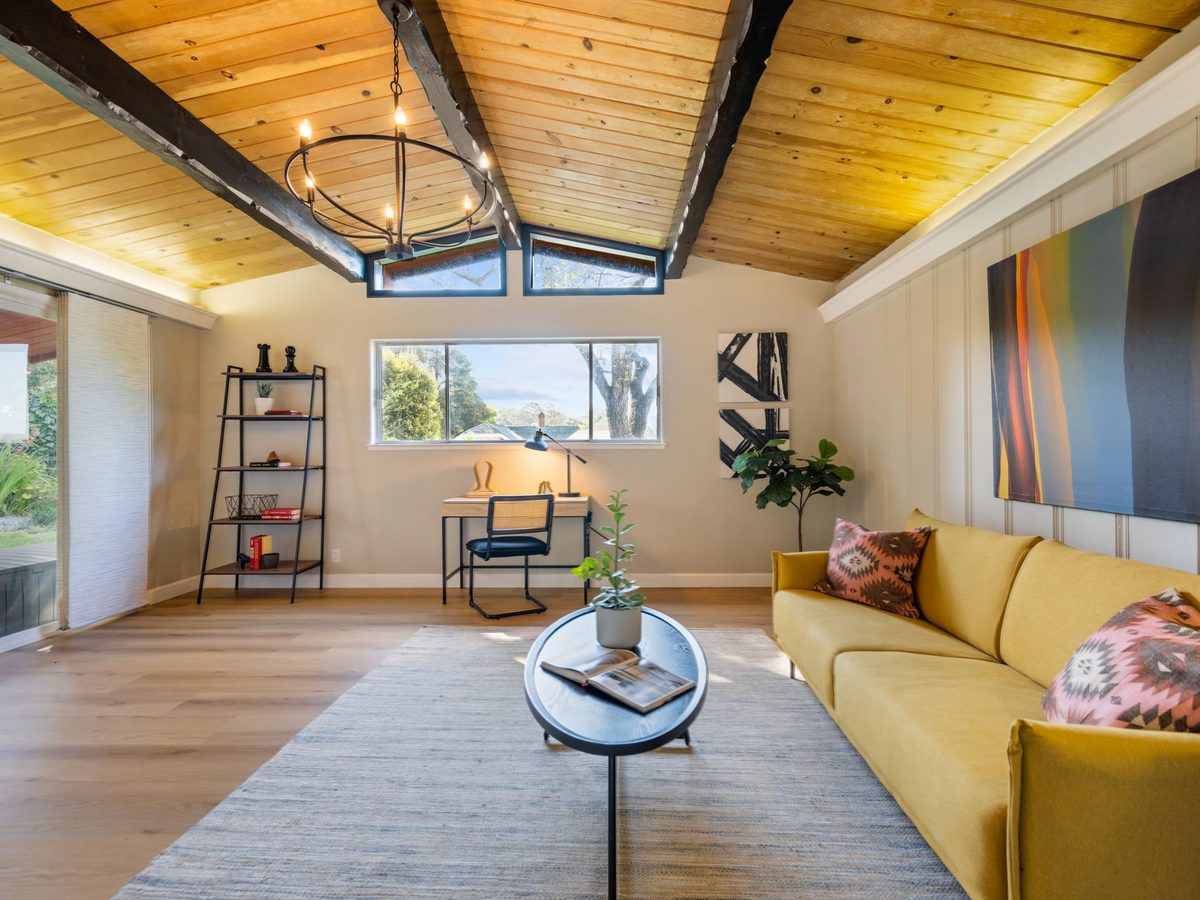 Staged living room with a vaulted wood-plank ceiling, dark beams and a mustard sofa