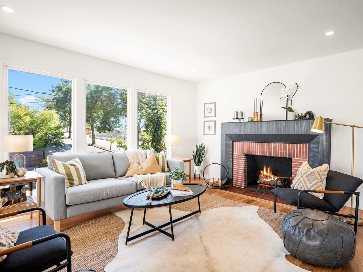 Living room with large windows, a gray sofa and a dark-surround brick fireplace